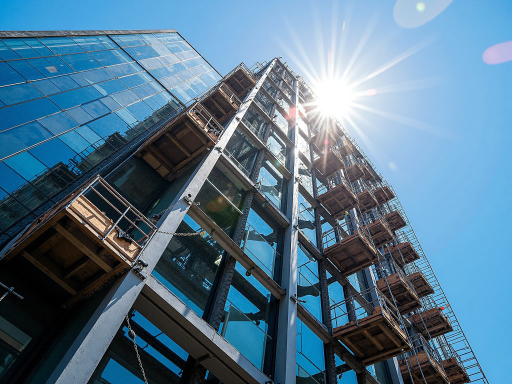 High rise building facade showing curtain wall system, professional maintenance worker on scaffolding platform, urban cityscape background